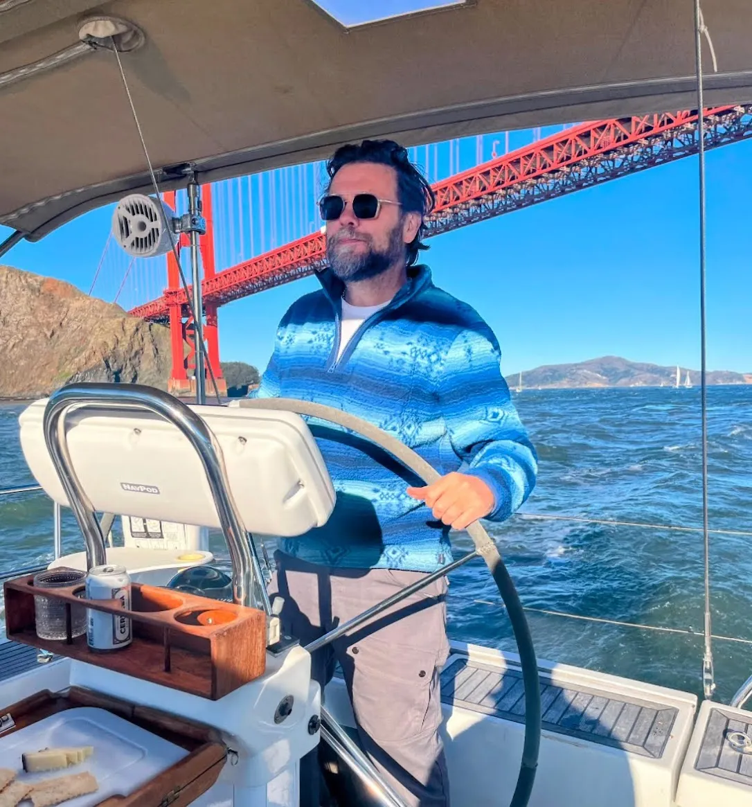 Andre at the helm of a sailboat on San Francisco Bay, with the Golden Gate Bridge behind him